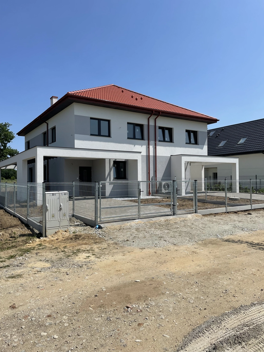 Budowa domów pod klucz nowoczesny dwukondygnacyjny dom z białą elewacją, czerwonym dachem i ogrodzeniem