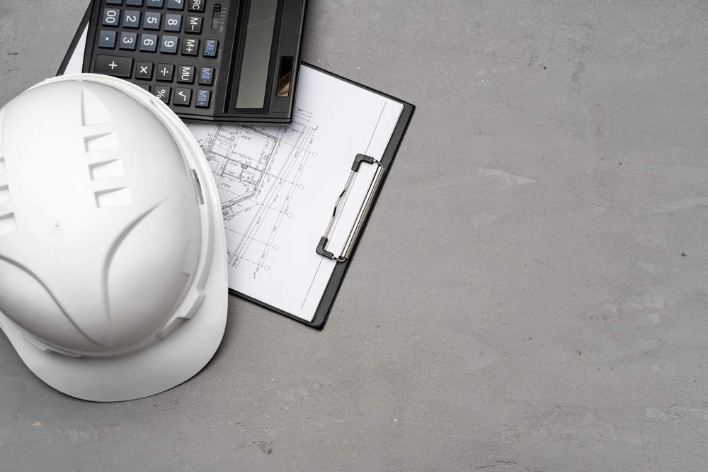Kask ochronny i kalkulator obok planu architektonicznego na clipboardie – kosztorys budowlany