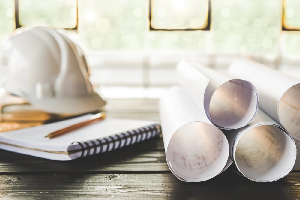 Kask ochronny, zwinięte plany budowlane i notes z ołówkiem na stole – Adaptacja projektu